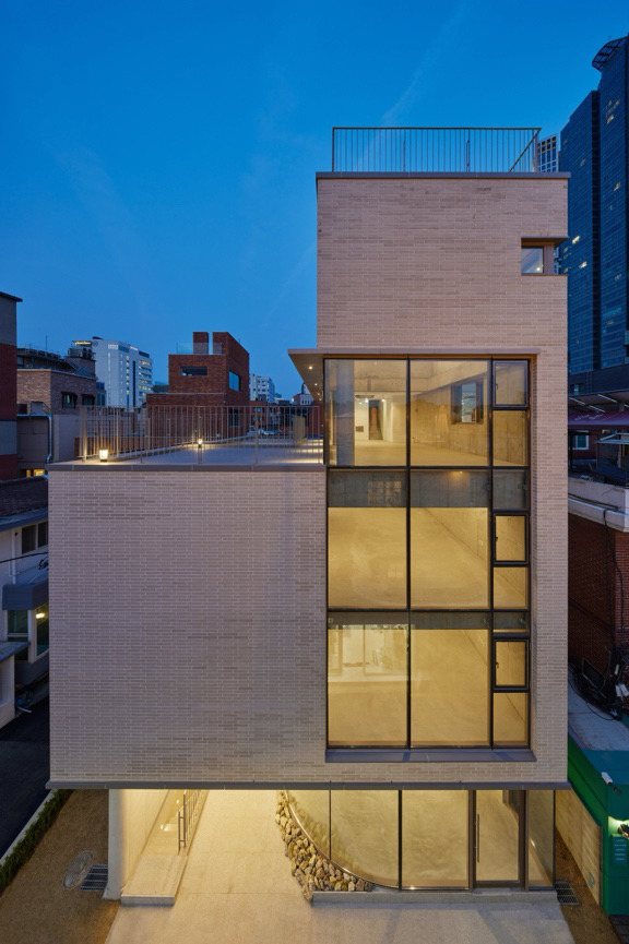 저녁의 클럽하우스 외관 — 벽돌 입면과 불이 켜진 통창